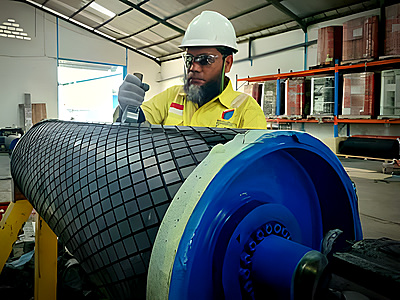 Technician installing REXWRAP diamond pattern rubber lagging on a conveyor pulley