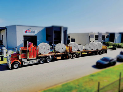 Flatbed truck transporting large finished conveyor pulleys from a Rexline manufacturing facility