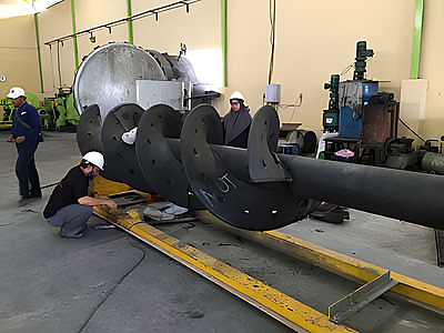 Workers fabricating a large screw feeder shaft with wear-resistant lining in a workshop