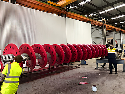 Large red screw feeder shaft being fabricated for nickel mining operations